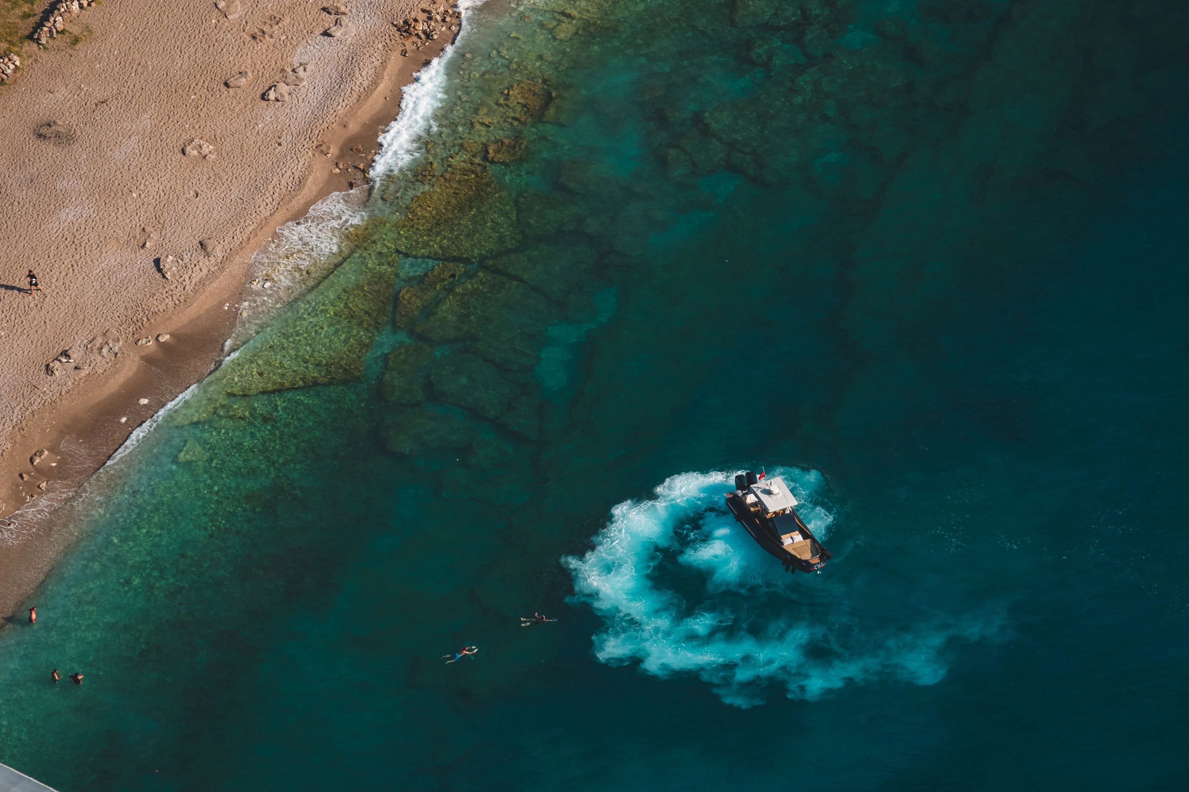 Vista aérea de uma praia, com água transparente e um barco junto à costa